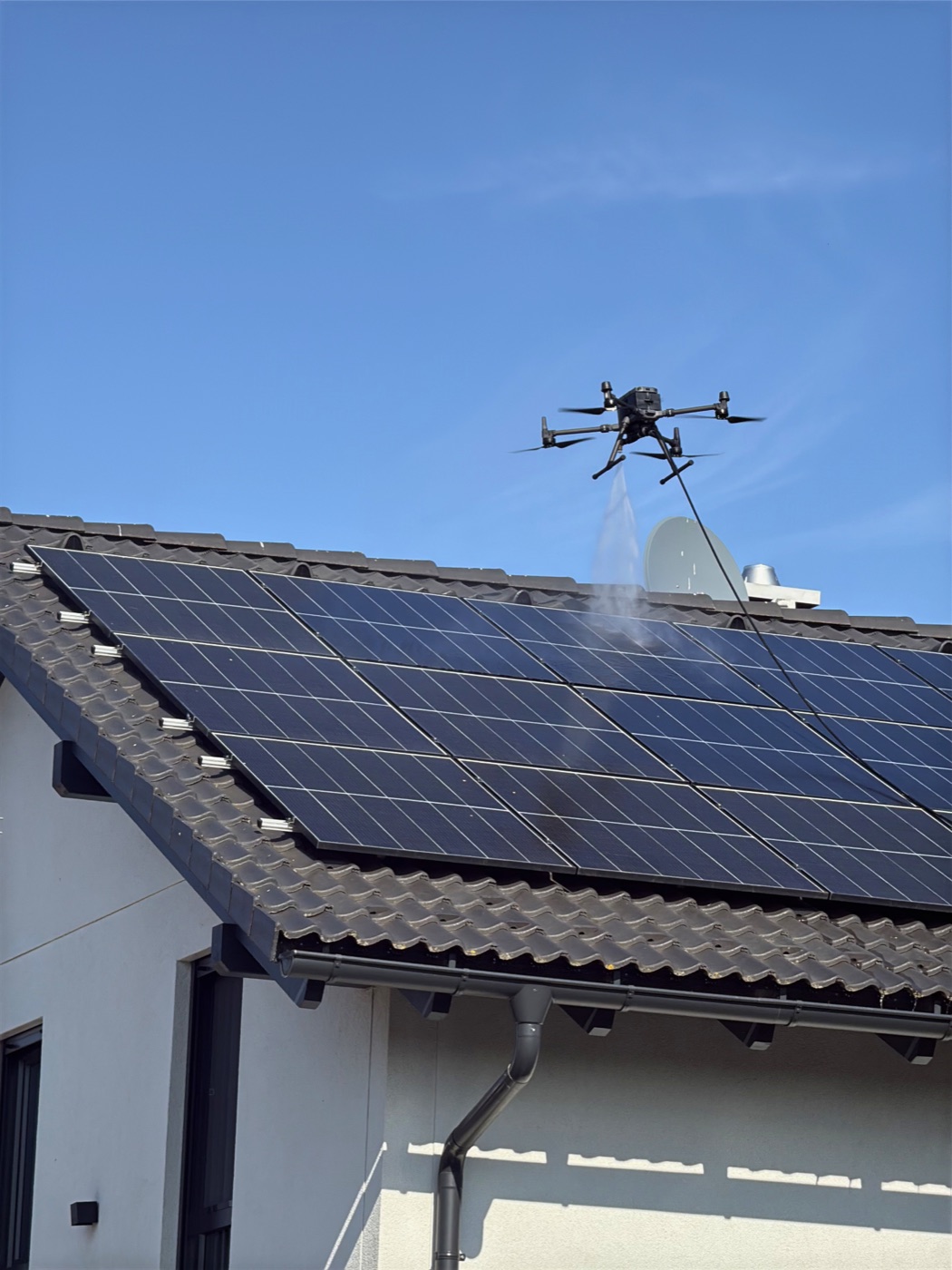 Reinigungsdrohne von First Drone besprüht eine Photovoltaikanlage auf einem Wohnhausdach mit Osmosewasser